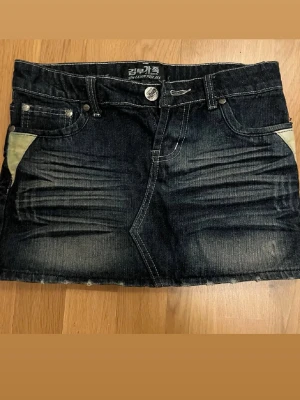 Mörkblå jeanskjol - Säljer en mörkblå jeanskjol med coola slitningar och  fickdetaljer fram och bak. Kjolen är kort och lågmidjad.