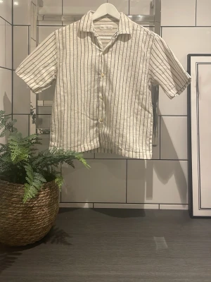 Randig kortärmad skjorta från Zara - Snygg kortärmad skjorta från Zara i beige med svarta vertikala ränder. Skjortan har klassisk krage, knappar framtill och är gjord i 100% bomull. Perfekt för en chill och stilren look under varma dagar. Jag kan såklart gå ner i pris + Svarar på alla era frågor ✨