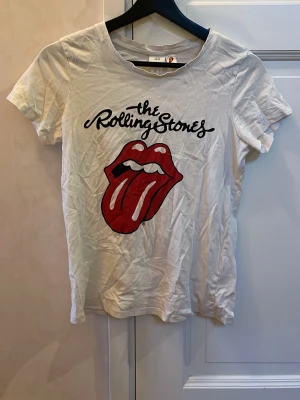 Rolling Stones t-shirt från H&M XS - Vit t-shirt från H&M med Rolling Stones-tryck och ikonisk röd tunga framtill. Modellen är klassisk med rund hals och korta ärmar. Perfekt för dig som gillar bandmerch och vill ha en cool och avslappnad stil. Materialet är mjuk bomull.