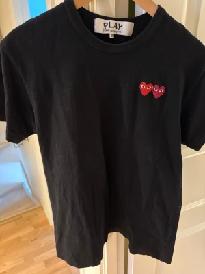 Svart Comme des Garçons Play t-shirt - Svart t-shirt från Comme des Garçons Play i storlek M. Klassisk rund hals och korta ärmar. På bröstet finns två broderade röda hjärtan med ögon, en ikonisk detalj från Play-kollektionen. Tillverkad i mjuk bomull som är skön mot huden. Jag säljer denna då den börjar bli för liten för mig.