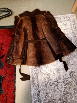 Brun pälsjacka med bälte - Säljer en brun pälsjacka med snyggt bälte i midjan och knappar framtill. Jackan har lång ärm och är fodrad med brunt tyg på insidan. Perfekt för dig som vill sticka ut med en cool vintage-look.