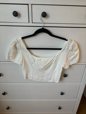 Vit croppad blus - Säljer en vit croppad blus från FB Sister i storlek M. Toppen har puffiga korta ärmar, fyrkantig halsringning och smockad rygg för extra komfort. Materialet känns mjukt och lätt, perfekt för varmare dagar. Snygg och enkel att matcha med jeans eller kjol.