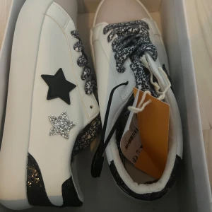 Vita sneakers med stjärndetaljer - Snygga vita sneakers med svart och silverglittrig stjärna på sidan. Skorna har svartglittrig häl, svartvita snören och leopardmönstrad plös. Perfekta för dig som vill sticka ut med coola detaljer. Helt nya. Ord pris 499 kr