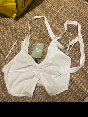Vit omlott linnetopp från H&M - Säljer en fräsch vit omlott linnetopp från H&M med smala axelband och snörning framtill. Toppen är ärmlös och har en lätt croppad passform. Materialet är en mix av linne och viskos som känns svalt och skönt mot huden. Perfekt för varma dagar!