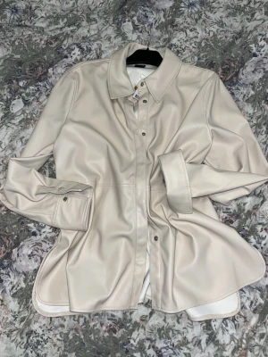 Beige overshirt från Gina Tricot - Snygg beige overshirt från Gina Tricot i mjukt material. Jackan har klassisk krage, tryckknappar framtill och vid ärmslut. Perfekt att styla lager på lager och ger en clean vibe till din outfit. Färg: beige.  Passar dig som gillar minimalistiskt och trendigt.