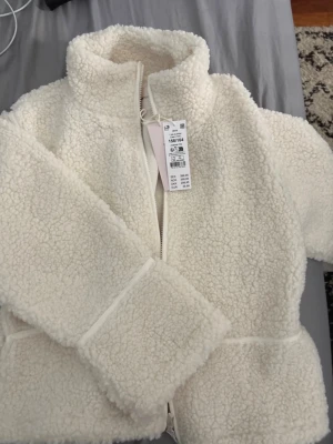 Vit teddyjacka från Gina Tricot - Mysig vit teddyjacka från Gina Tricot i storlek 158/164. Jackan har hög krage, dragkedja framtill och är gjord i fluffigt teddy-material som håller dig varm. Perfekt för dig som gillar en enkel men trendig look.
