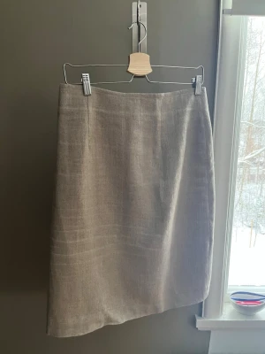 Linnekjol från Jordnära - Säljer en stilren beige kjol från Jordnära, designad av Kerstin Bendelin. Kjolen är rak i modellen, tillverkad i linne och har en diskret dragkedja bak. Perfekt för dig som gillar minimalistisk och naturlig stil. Använd ett fåtal gånger 100% linne.