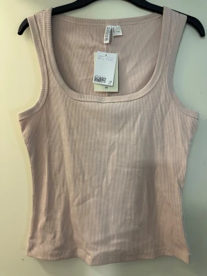 Beige ribbad linnetopp från H&M Divided strl: L - Säljer en beige ribbad linnetopp från H&M Divided i storlek L. Toppen är ärmlös med breda axelband och har en rundad halsringning. Materialet är mjuk och stretchig bomull med 5% elastan för extra komfort. Perfekt för sommaren och enkel att matcha med jeans eller shorts.