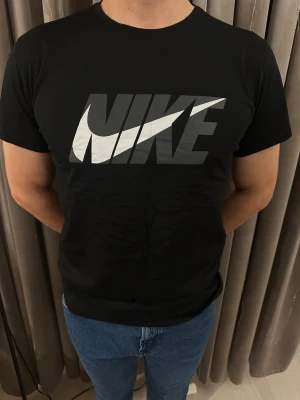 Svart Nike t-shirt med stor logga - Snygg svart t-shirt från Nike med stor, grå och vit logga över bröstet. Klassisk rund hals och korta ärmar. Skön passform och tillverkad i mjuk bomull som känns bekväm hela dagen. Perfekt för dig som gillar sportiga och stilrena plagg.