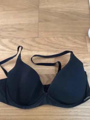 Svart T-shirt BH från h&M, storlek 75 C  - Svart BH med justerbara axelband. Klassisk form med bygel och mjuk känsla. Materialet är polyester och BH:n har en enkel design utan mönster eller extra detaljer. Perfekt för dig som gillar stilrena underkläder.