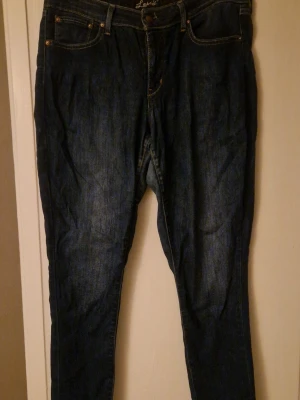 Levi's 501 mörkblå jeans, storlek 30 - Mörkblå Levi's 501 jeans med klassisk femficksdesign och kontrastsömmar. Jeansen har rak passform och är tillverkade i slitstarkt bomullsjeansmaterial. Snygga detaljer med metallknapp och broderad logga i midjan. Lite slitna I grenen och insida lår. Tror det är storlek 30, det är den enda siffran jag hittar 😀