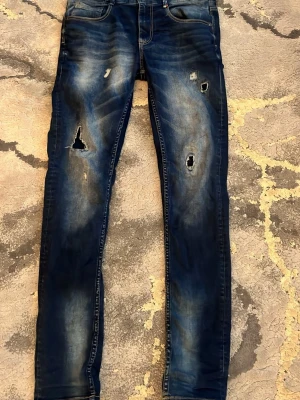 Mörkblå skinny jeans med slitningar - Säljer ett par mörkblå skinny jeans med coola slitningar och hål på framsidan. Jeansen har klassisk femficksdesign och är tillverkade i stretchigt denimmaterial för skön passform. Perfekt för dig som gillar en edgy streetstil.