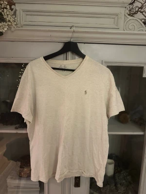 Vit v-ringad t-shirt från Polo Ralph Lauren - Vit t-shirt från Polo Ralph Lauren med v-ringning och klassisk logobroderi på bröstet. T-shirten är kortärmad och har en clean, enkel design som funkar till allt. Tillverkad i mjuk bomull för skön känsla hela dagen.