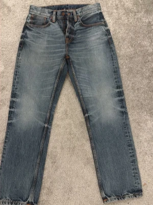 Nudie Jeans Sleepy Sixten blå jeans - Säljer ett par Nudie Jeans Sleepy Sixten i klassisk blå tvätt med snygga fades och orangea sömmar. Modellen har raka ben och fem fickor, tillverkade i 100% ekologisk bomull. Perfekt för dig som gillar en chill och tidlös jeansstil.