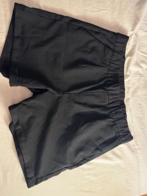 Svarta shorts med elastisk midja - Säljer ett par svarta shorts med elastisk midja och enkel design. De är tillverkade i ett mjukt bomullsmaterial och har en normal passform. Perfekta för varma dagar och chill häng.