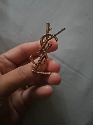 Brosch - Bilden visar ingen väst utan ett smycke eller brosch i guldton. Ingen information om väst kan ges.