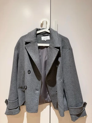 Oanvänd Grå kavajjacka från Bubbleroom - Snygg grå kavajjacka från Bubbleroom i storlek S passar även M. Jackan har bred krage, dubbla knappar framtill och dekorativa knappar vid ärmsluten. Materialet är mjukt och känns som ullblandning, med slät fodrad insida. Perfekt för dig som gillar stilrena och klassiska plagg. Helt ny jacka! Nypris 1099 jag säljer den för 599