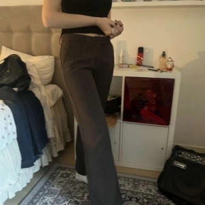 Bruna randiga kostymbyxor med bootcut - Snygga bruna kostymbyxor med tunna vita ränder och bootcut-silhuett. Byxorna har bälteshällor, fickor fram och bak samt klassisk stängning. Perfekta för dig som gillar en dressad men chill look.