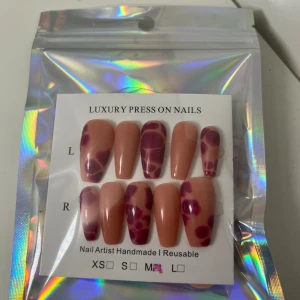 Lyxiga press-on naglar med mönster - Säljer ett set lyxiga press-on naglar i medium storlek. Naglarna har en nude bas med vinröda och lila abstrakta mönster. De är formade i en elegant coffin-stil och är återanvändbara. Perfekt för dig som vill ha snygga naglar snabbt! Obs Naglarna är handgjorda utav mig därav priset 