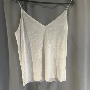 Silvergrått sammetslinne med smala axelband - Säljer ett silvrigt linne från Gina Tricot i mjuk sammet med smala axelband och v-ringning fram ich bak. Enkel och stilren design som ger en lyxig känsla.