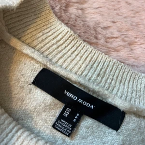 Beige stickad tröja - Mysig beige stickad tröja från Vero Moda i storlek S. Tröjan har rund halsringning, ribbade muddar och lång ärm. Perfekt för lager-på-lager under kyliga dagar och enkel att matcha med jeans eller kjol.