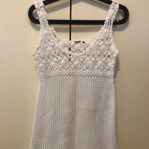 Vit virkad topp  - Superfin vit virkad topp med breda axelband och vackert mönstrad överdel. Perfekt för varma dagar och ger en bohemisk känsla. Klänningen är ärmlös och har en luftig, kort modell som passar perfekt till sommaren.