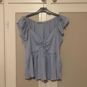 Ljusblå blus  - Supersöt ljusblå blus från Lager157 med volangärmar och knytning framtill. Blusen har v-ringning och är luftig, superskön på! Använd fåtal gånger så i fint skick!