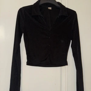 Svart croppad blus från HM - Materialet är mjukt och glansigt. Liknade Microtyg. 