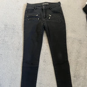 Svarta skinny jeans med dragkedjor - Svarta skinny jeans från Denim 1953 med flera coola dragkedjor framtill och klassiska bakfickor. Jeansen har låg midja och är tillverkade i stretchigt denim för en tight passform. 
