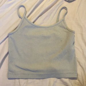 Ljusblå ribbad linnetopp från New Yorker - Supersöt ljusblå linnetopp från New Yorker i storlek XS. Toppen är ribbad med smala axelband och croppad passform, perfekt för varma dagar. Materialet är mjukt och stretchigt, troligtvis bomull eller syntet. Enkel och stilren design som är lätt att matcha med allt.
