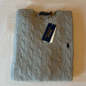  Ljusgrå kabelstickad tröja Polo Ralph Lauren - Skit snygg Kabelstickad ljusgrå tröja från Polo Ralph Lauren. Tröjan är i mjuk bumull och är perfekt för lager-på-lager under hösten och vintern. Helt ny men passade inte mig.