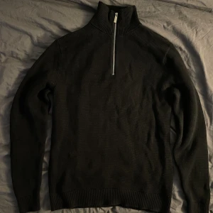 Svart half zip stickad tröja Selected Homme - Svart stickad tröja från Selected Homme med hög krage och half zip-dragkedja. Tröjan är i 100% ekologisk bomull och har en clean, klassisk look med ribbade muddar och lång ärm. Perfekt för lager-på-lager under höst och vinter.