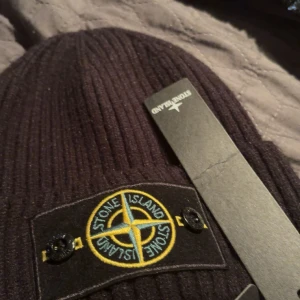 Svart ribbad mössa från Stone Island - Säljer en svart ribbstickad mössa från Stone Island med den klassiska loggan framtill. Mössan är i mjukt material och har en snygg, enkel design som passar perfekt till kalla dagar.