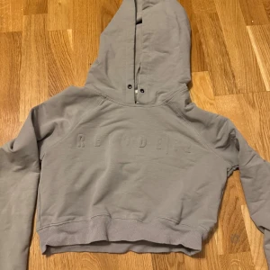 Beige croppad hoodie från Relode - Snygg beige croppad hoodie från Relode med broderad logga framtill. Tröjan har huva, långa ärmar och ribbade muddar. Perfekt för en chill och sportig look. Mjuk och skön i bomullsmix. Har tyvärr tappat bort snörerna.
