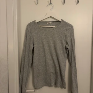 Grå basic långärmad tröja - Enkel och stilren grå långärmad tröja i mjuk bomull. Perfekt att ha som basplagg och funkar året runt. Tröjan har rund halsringning och en normal passform som är lätt att matcha med allt.
