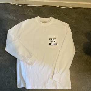 Vit långärmad tröja från DEPT de la GALERIE - Vit långärmad tröja från DEPT de la GALERIE med svart tryck både fram på bröstfickan och stort på ryggen. Tröjan har rund hals, muddar vid ärmslut och är gjord i mjuk bomull. Perfekt för en clean och stilren look. ( Oanvänd ) 