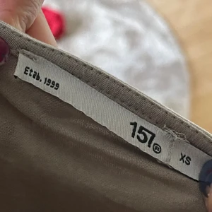 Beige topp från 157 XS - Säljer en enkel och stilren beige topp från 157 i storlek XS. Toppen har rund hals och är kortärmad med en tight passform som sitter snyggt mot kroppen. Perfekt att matcha med jeans eller kjol för en clean look.