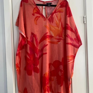 Blommig korallröd strandklänning från Lindex - Säljer en luftig strandklänning från Lindex i korallrött med stora blommiga mönster i rött och orange. Klänningen har v-ringning, korta ärmar och en snygg öppen detalj i ryggen. Perfekt för sommarens varma dagar och har en avslappnad passform. Mått Över bröstet: ca 80 cm Längd från axeln och ner: ca 86 cm  100% polyester   Kommer från ett djur och rökfritt hem.