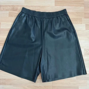 Nya. Svarta loose skinnshorts med resår - Snygga svarta shorts i skinnimitation med loose fit och elastisk midja. De har en enkel, stilren design utan synliga detaljer eller mönster, vilket gör dem riktigt cleana. Perfekta för dig som gillar en edgy och modern vibe. Ordpris 399kr, nu 200kr ej prutbar.