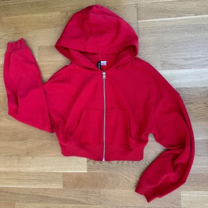 Röd Croppad Hoodie med dragkedja - Röd croppad hoodie från H&M med huva och dragkedja framtill. Tröjan har långa ärmar och två fickor framtill. Är i storlek XS, men jag tar på mig S/M och den sitter bra på mig! 