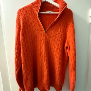 Orange stickad tröja med half zip - Säljer en orange stickad tröja från Davida med kabelstickat mönster och ribbad krage. Tröjan har en snygg half zip-dragkedja och långa ärmar. Perfekt för dig som vill ha en färgstark och mysig look.
