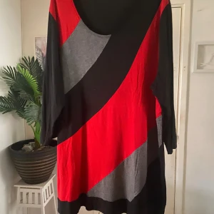 Röd och svart mönstrad klänning - Cool kortklänning /tunika med breda diagonala block i rött, svart och grått. Klänningen har rund halsringning och trekvartsärmar. Mjuk och stretchig känsla, perfekt för dig som gillar färg och grafiska mönster.