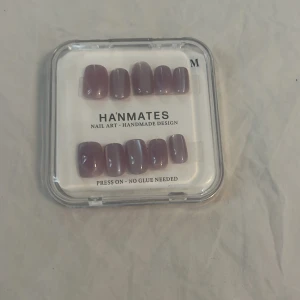Press on-naglar i lila från HANMATES - Snygga press on-naglar i en mjuk lila nyans med glansig finish. Kommer i en praktisk ask med tillbehör som nagelfil och pinne. Medium storlek, fyrkantig form och handgjord design. Inget lim behövs, bara att trycka på naglarna för en snabb och enkel look.