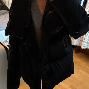 Svart pufferjacka från Soaked in Luxury - Säljer en svart pufferjacka från Soaked in Luxury med bred krage och oversized passform. Jackan är gjord i glansigt material och har tryckknappar framtill. Perfekt för kalla dagar när du vill vara både varm och snygg.