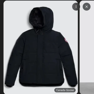 Svart Macmillan Parka från Canada Goose - Snygg svart Macmillan Parka från Canada Goose med klassisk design och diskret logga på ärmen. Jackan är vadderad och har långa ärmar, praktiska fickor och dragkedja framtill. Perfekt för kalla dagar när du vill hålla stilen.