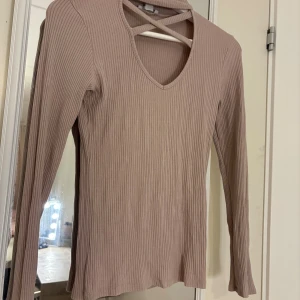 Gammelrosa ribbad långärmad topp Amisu - Säljer en gammelrosa ribbad långärmad topp från Amisu. Toppen har v-ringning och snygga korsade band i halsringningen som ger en extra detalj. Perfekt att styla med jeans eller kjol för en trendig look.