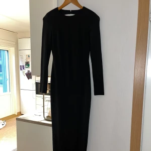 Svart långklänning med öppen rygg - Svart långklänning i stretchigt material med lång ärm, rund hals och en djup öppen rygg. Formad kroppen väldigt fint. Klänningen har en slits på sidan som ger extra edge. Perfekt för dig som vill sticka ut med en stilren och snygg look. Perfekt för nyår, haft den endast i några timmar🖤