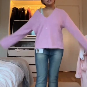 Ljusrosa kofta från Monki - Supermjuk ljusrosa kofta från Monki med v-ringning och knappar framtill. Koftan har en oversized passform, långa ärmar och är stickad i ett fluffigt material som känns riktigt cozy. Perfekt att slänga på sig när du vill vara både chill och söt. Storlek XS men sitter mer som S