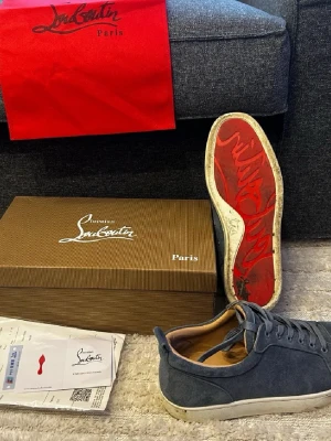 Blåa Christian Louboutin sneakers - Sulan har inga defekter bilden är tagen efter jag har varit i lera. Snygga blåa sneakers från Christian Louboutin med klassisk röd sula och ovandel i mocka. Skorna har rund tå, snörning och vit platt sula. Perfekta för dig som vill ha en stilren och lyxig look med en ikonisk touch.