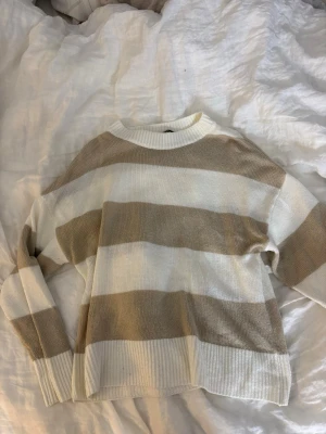 Randig beige och vit stickad tröja H&M - Mysig stickad tröja från H&M Divided i storlek S. Tröjan har breda beige och vita ränder, rund halsringning och ribbade muddar vid ärmslut och nederkant. Perfekt för lager på lager och chill vardagsstil.